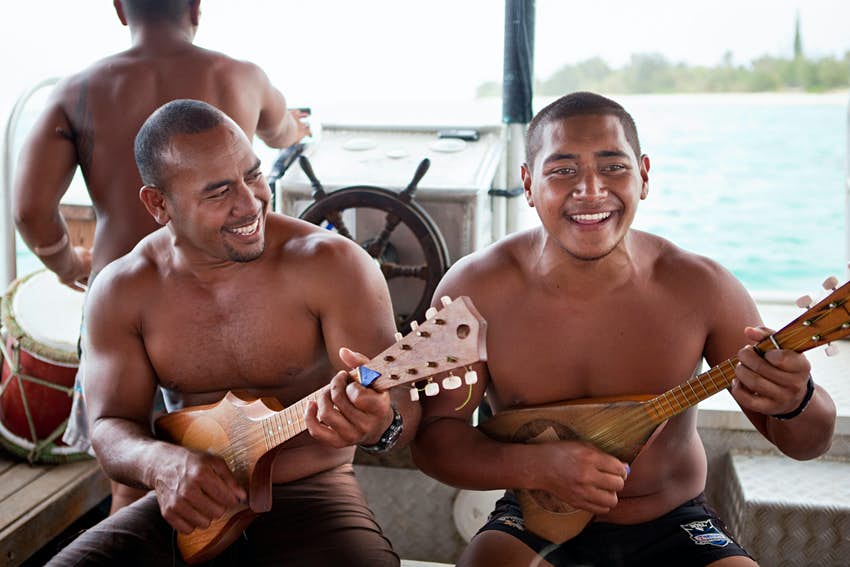 Guías tocando el ukelele a bordo de un barco con fondo de cristal en la laguna Muri, Rarotonga, Islas Cook.